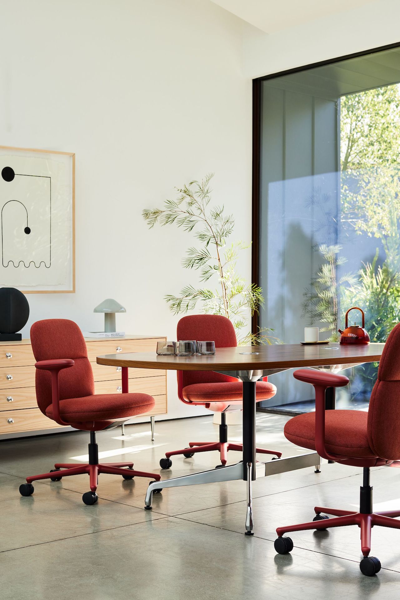 Three Asari chairs by Herman Miller in deep red surround a table in a room next to a sunny window.