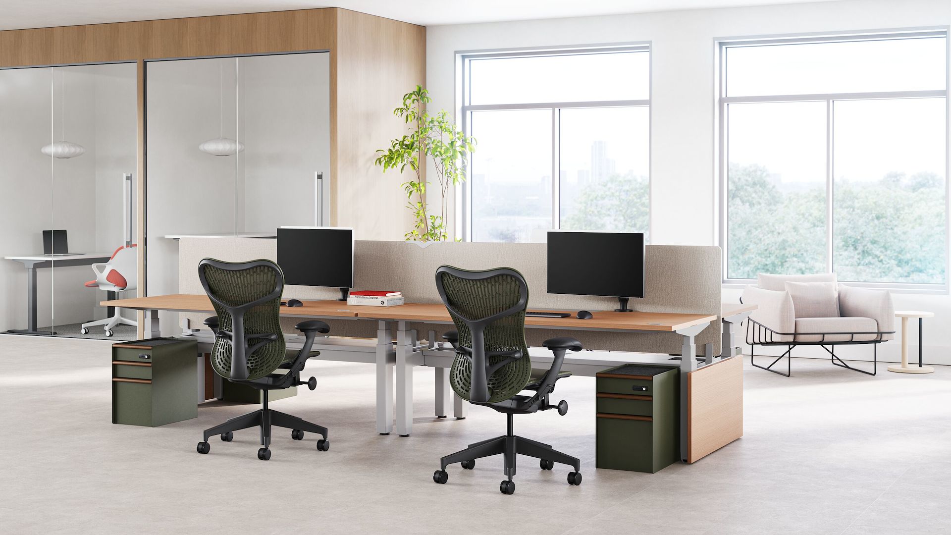 Two Mirra 2  chairs in with a graphite frame and olive butterfly back sit in front of a workstation in a touchdown space, with a room in the background.