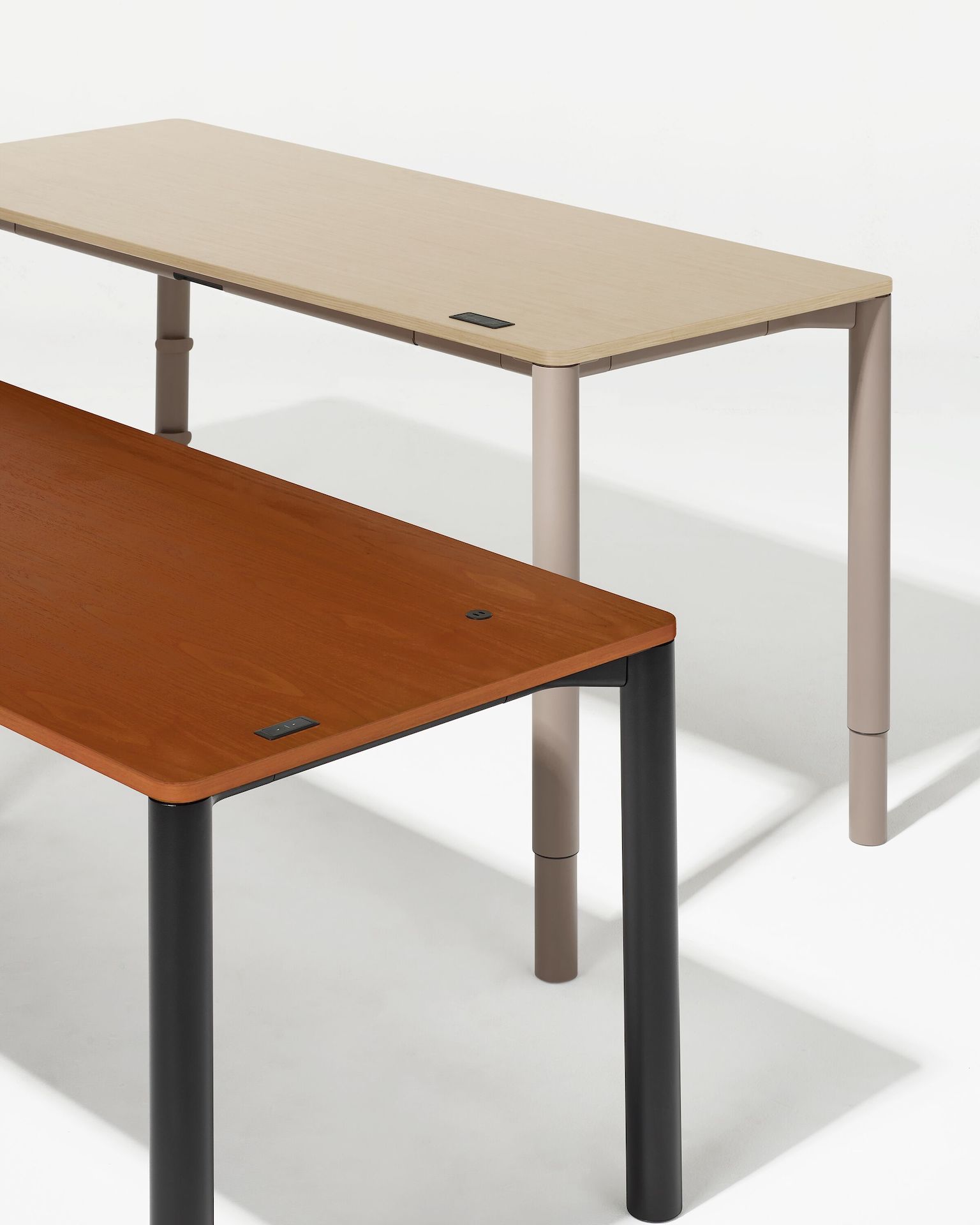 Two four leg height adjustable tables, one with a dark woodgrain surface and black legs and other  with a light woodgrain surface and light brown legs shown at standing posture.