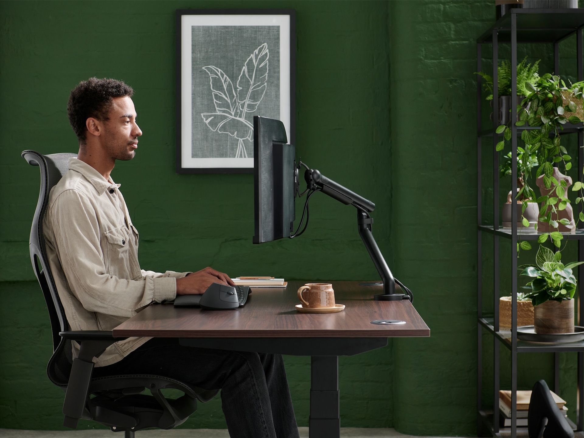 Person with brown curly hair using black Flo monitor arm in a working environment.