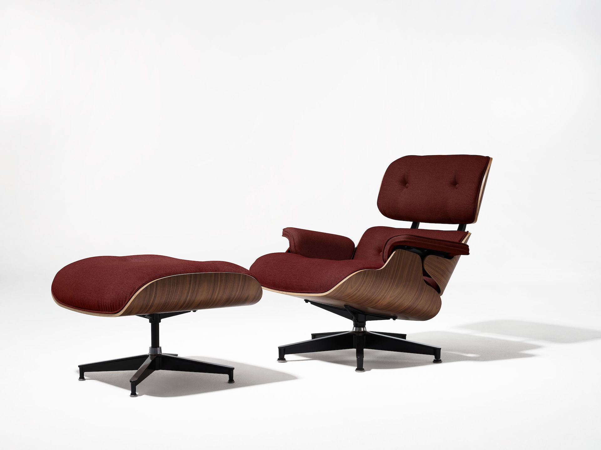Eames Lounge Chair and Ottoman with dark red fabric upholstery and walnut frame, viewed from an angle.
