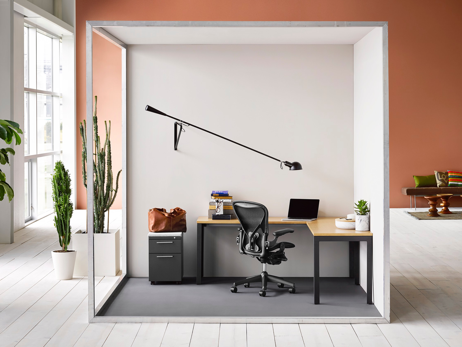 A semi-enclosed touchdown space containing an L-shaped Layout Studio surface, black Aeron office chair, and Tu storage pedestal.