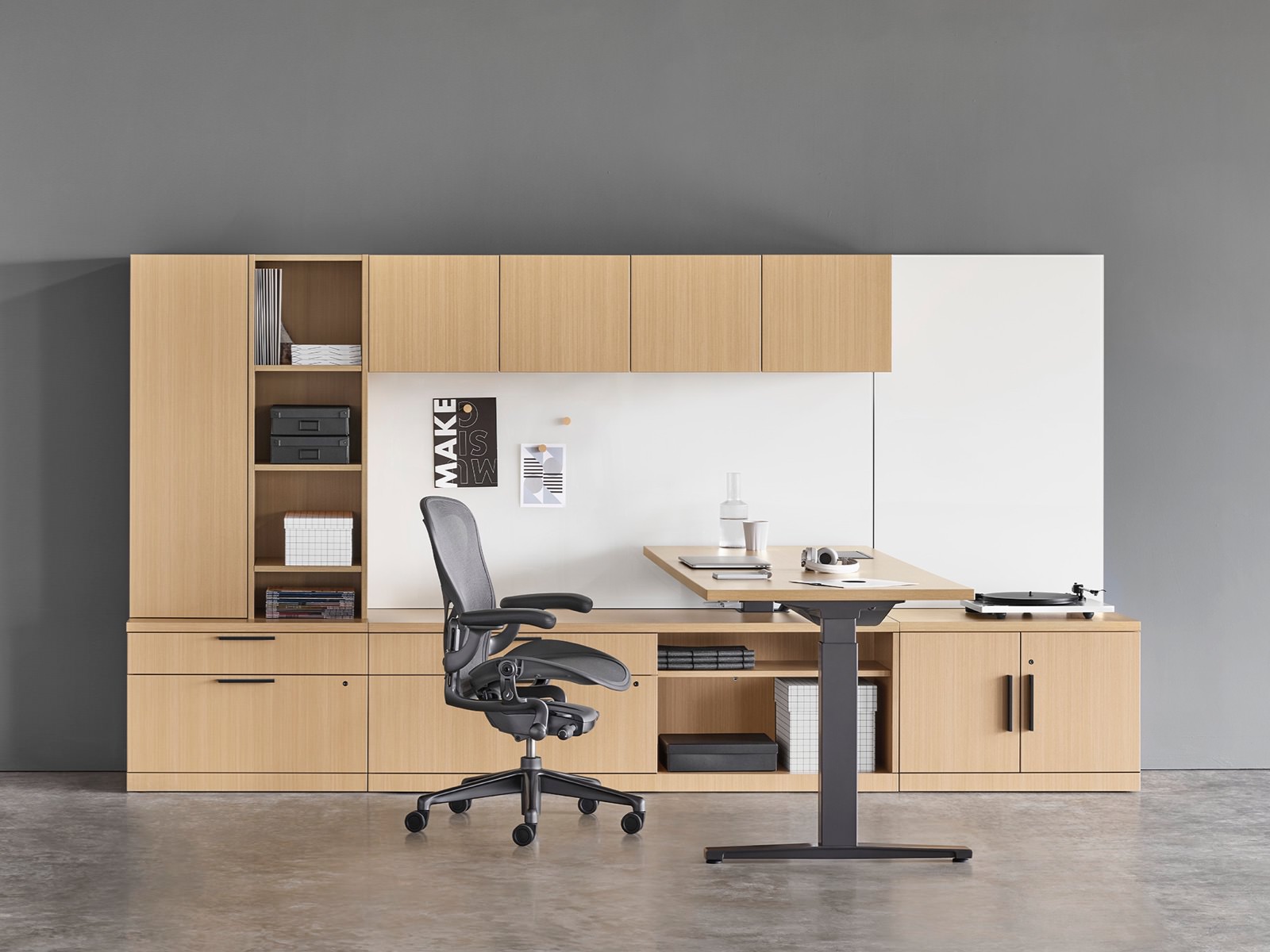 A Canvas Private Office with light wood storage, height adjustable desk, black Aeron chair, and light grey Striad lounge chair.