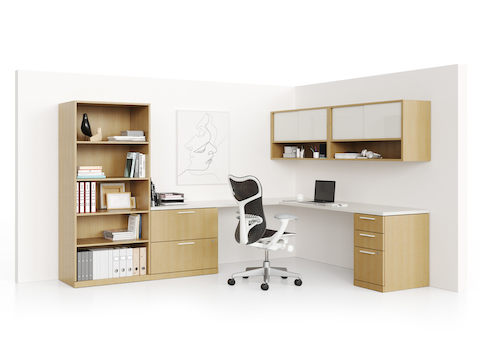 An L-shaped Canvas Private Office with a white desk surface and a bookcase, lateral file, pedestal, and overheads in a light wood finish.