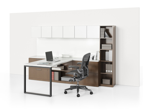 A Canvas Private Office consisting of a white peninsula surface, white overheads, a vertical bookcase, and file drawers in a dark wood finish.