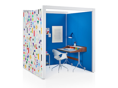 A three-sided Overlay space with blue tackable fabric interiors and colorful geometric pattern on the exterior wall with a chair and desk inside.