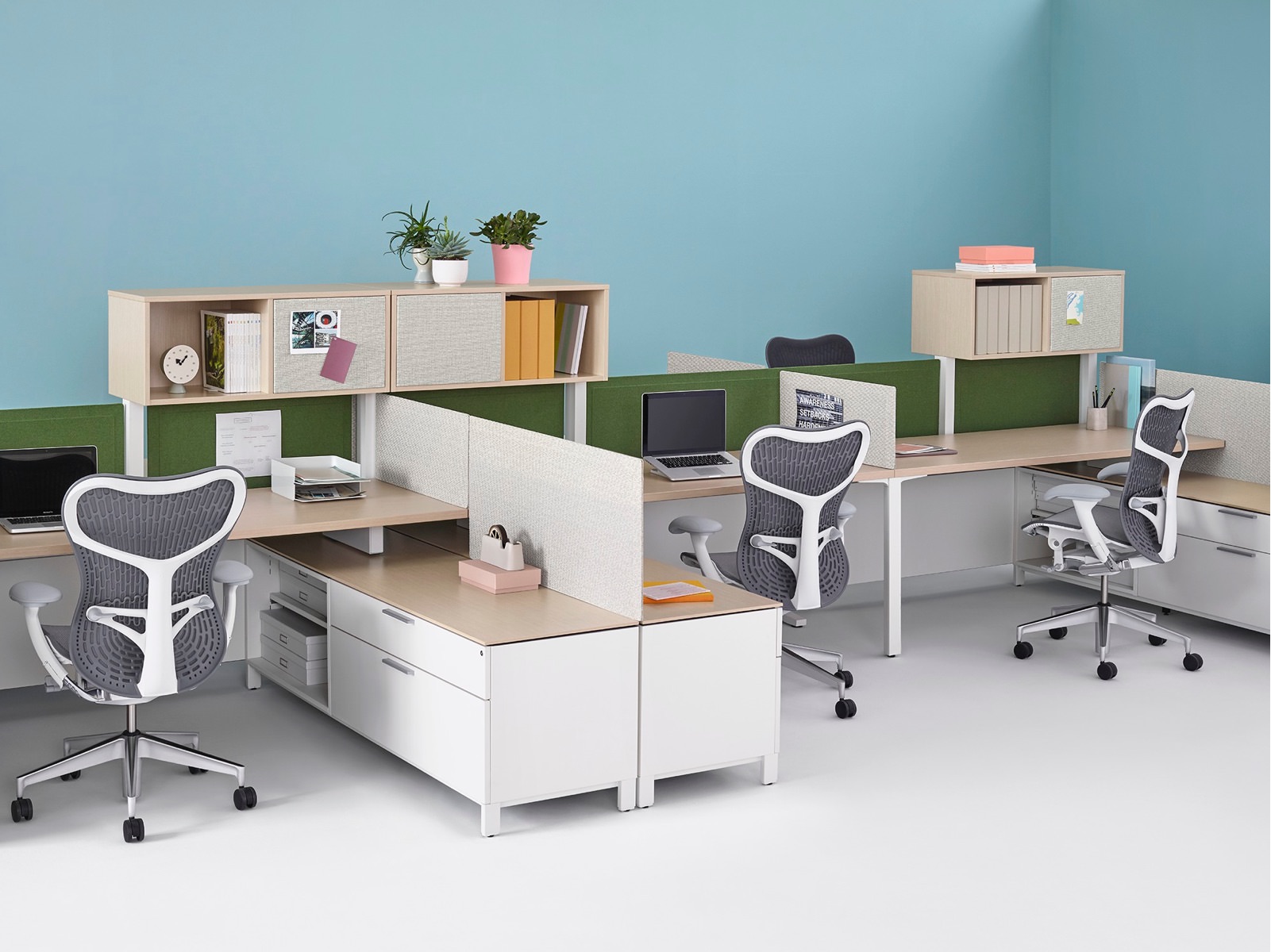 A cluster of L-shaped Canvas Dock workstations with upper and lower storage, green and ivory Pari privacy screens, and gray Mirra 2 office chairs.