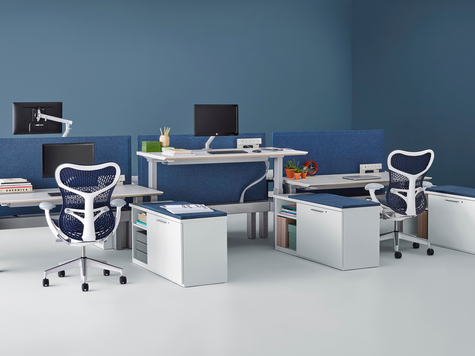 A benching configuration of Renew Link workstations with desks positioned at different heights and dark blue Pari privacy screens.