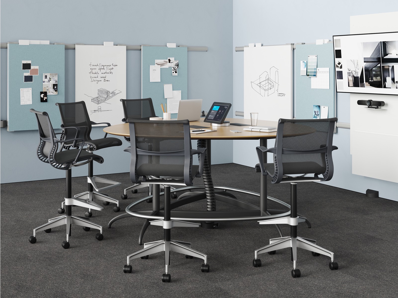 A meeting room setting featuring an Exclave table with five black Setu Stools in front of a monitor and Exclave display elements.