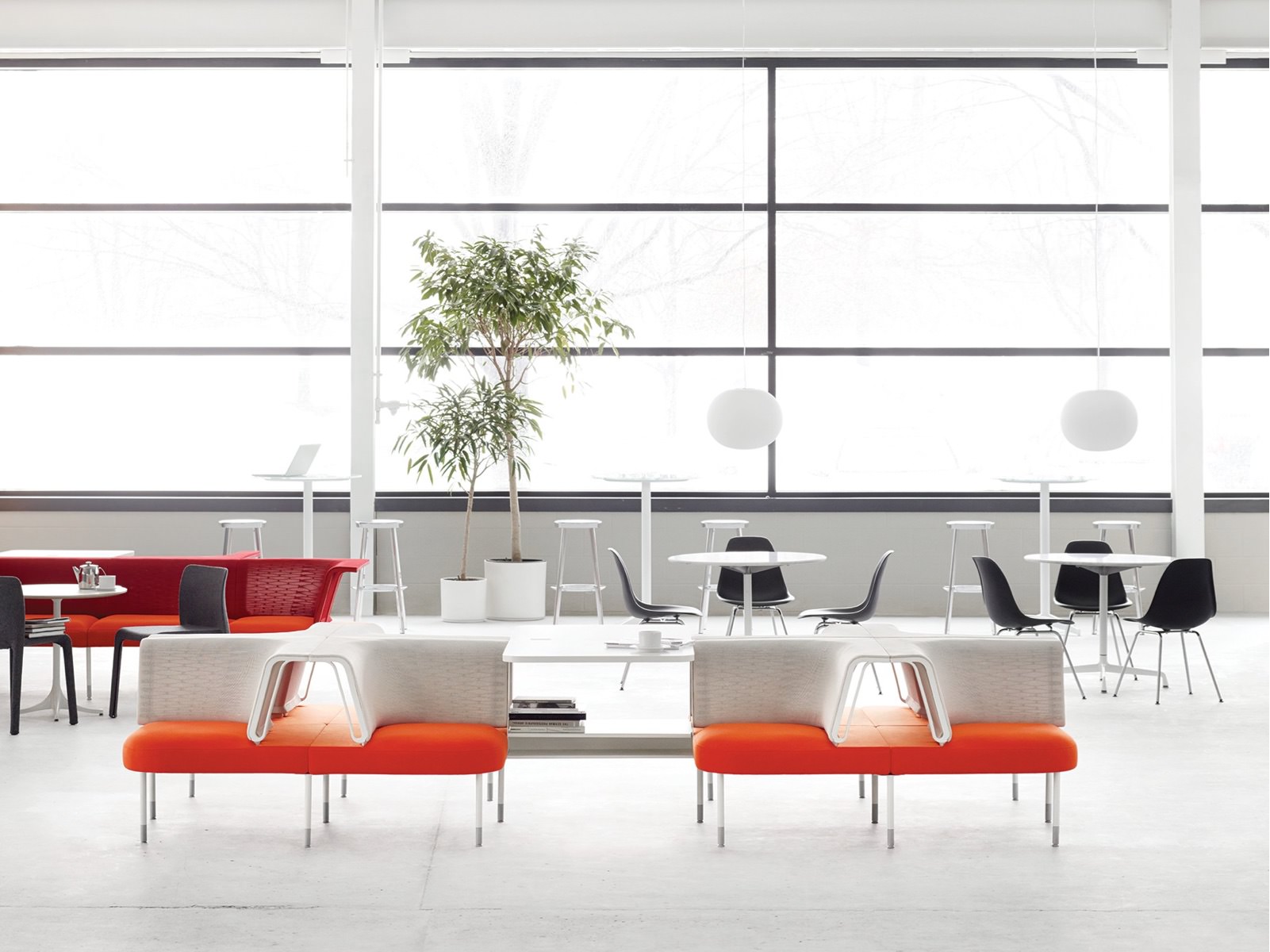 A gathering space with multiple interaction areas, including round tables, a counter, and Public Office Landscape social chairs in red, white, and orange.