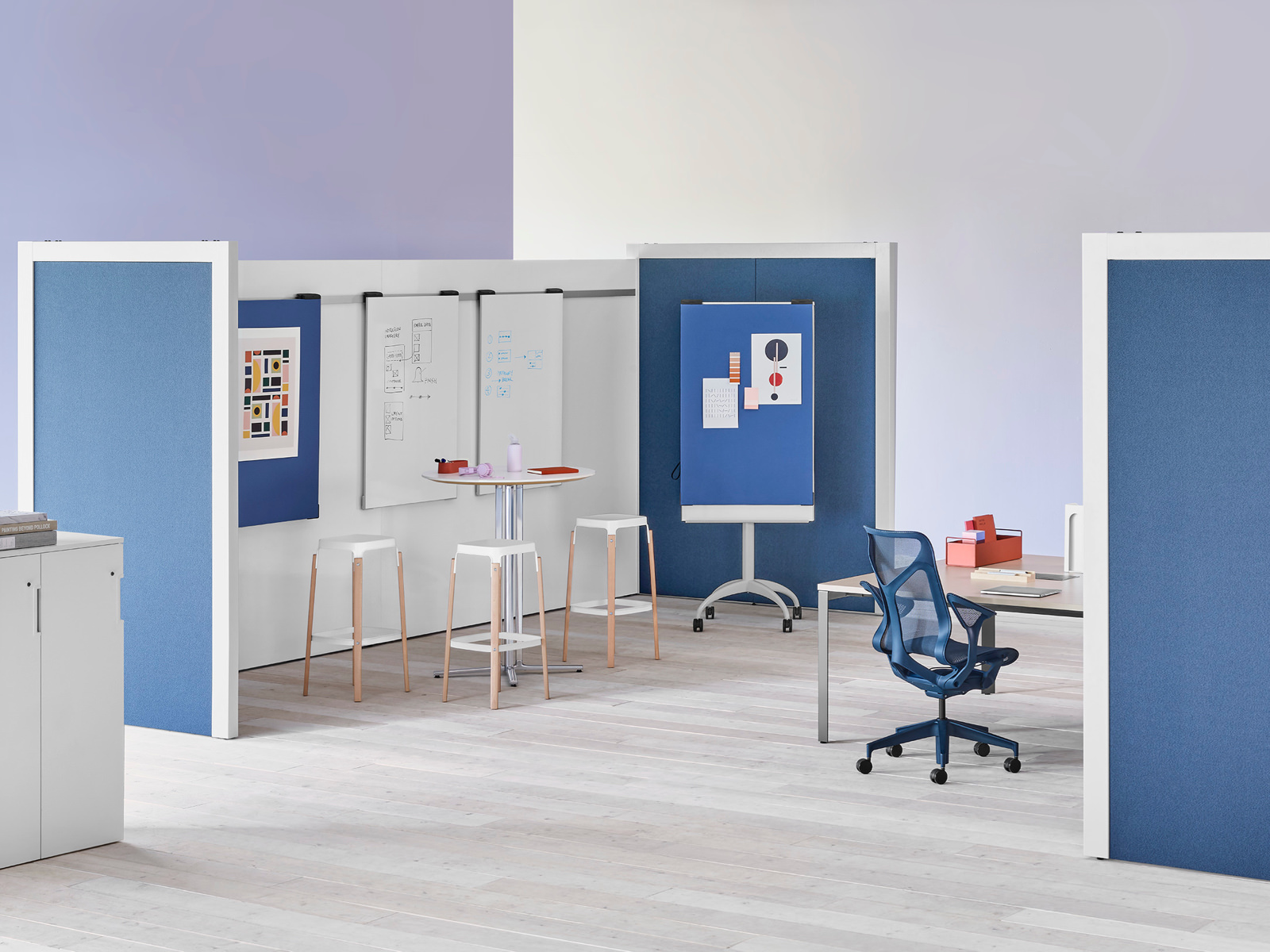 Two Overlay room dividers placed across each other with tables and chairs in between with markerboards in the interior and dark blue fabric on the exterior.