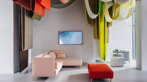 A Colourform sofa with pink upholstery and an ottoman with red quilted upholstery in a lounge. Brightly-colored bolts of fabric hang from the ceiling.