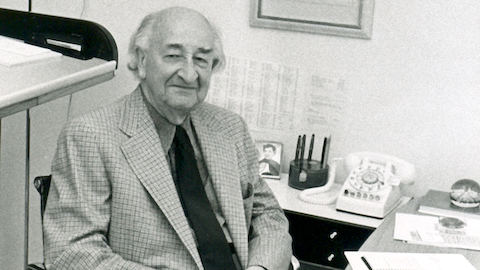 Un ritratto di D.J. De Pree seduto alla scrivania su una sedia Aluminum Group Eames.