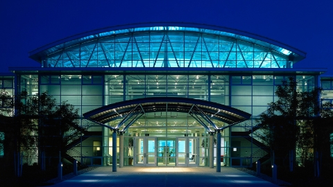 An outdoor photograph of the Herman Miller Greenhouse factory at night, lit from the inside.