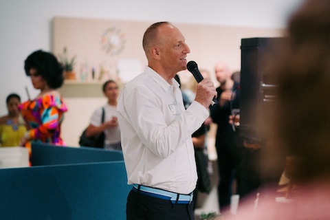 A man in a white shirt speaks into a microphone.