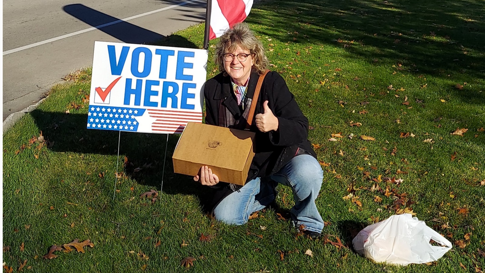 A woman kneeling near voting flag with a thumbs up.