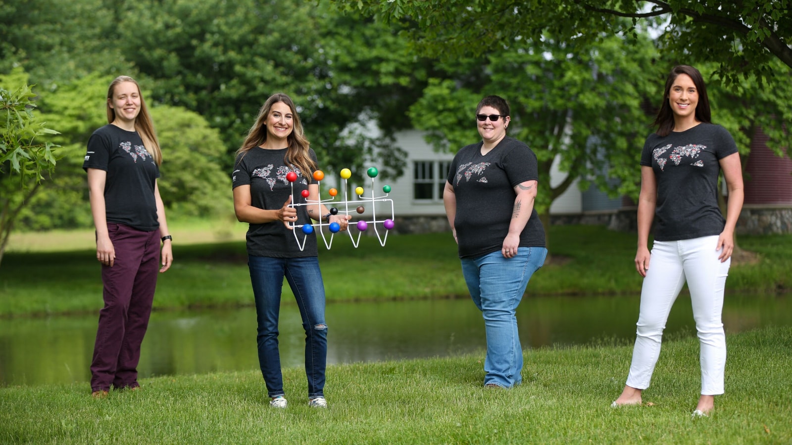 Four employees standing on a lawn holding an Eames Pride Hang-It-All.