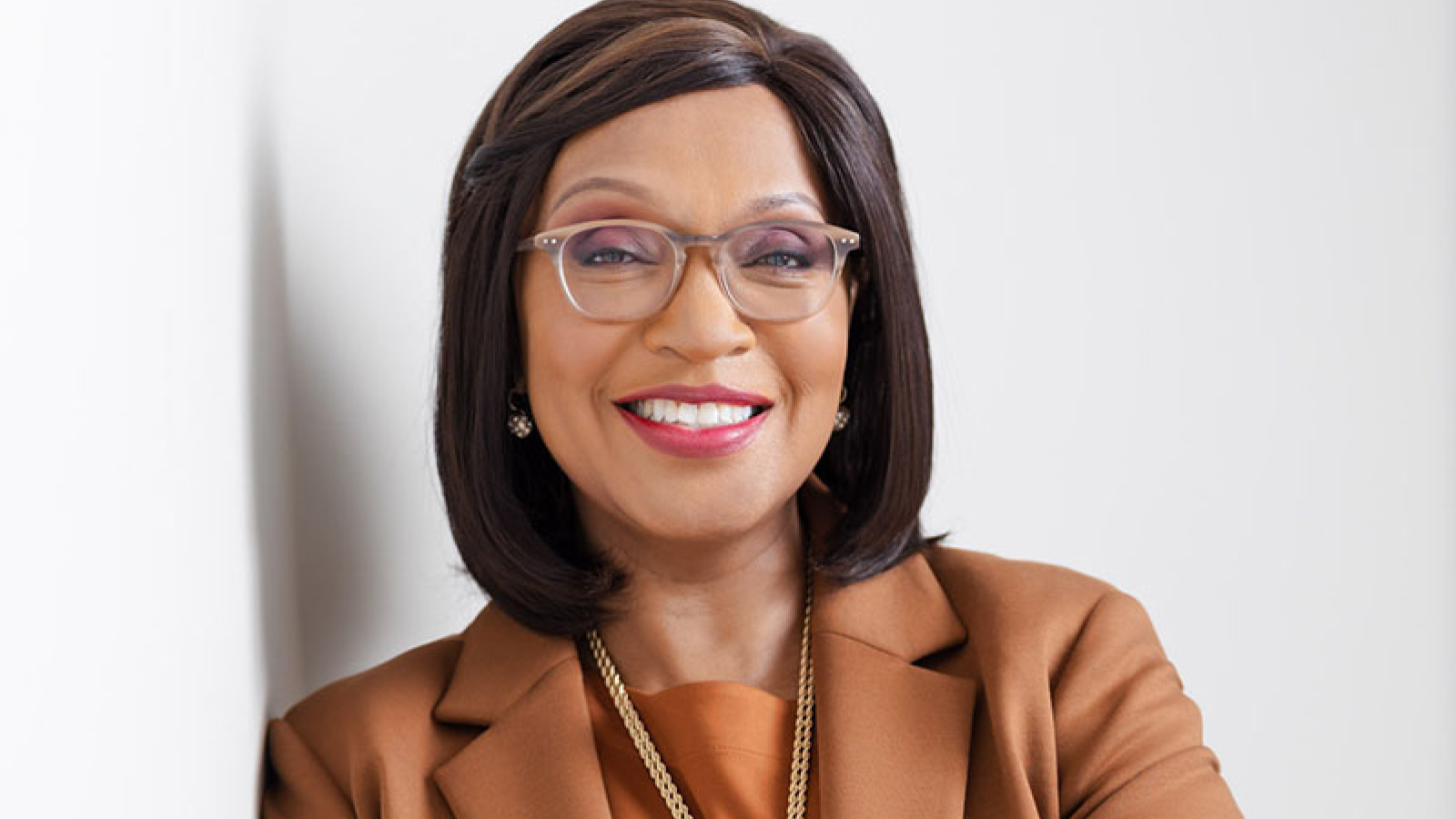 Herman Miller's VP of diversity, equity, and inclusion leaning against wall smiling with arms crossed. Herman Miller's VP of diversity, equity, and inclusion leaning against wall smiling with arms crossed.