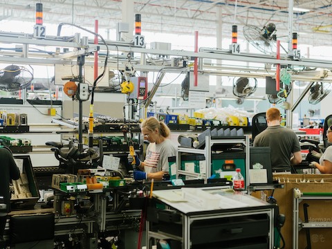 A man and a woman work on an assembly line assembling chairs as they move from one station to the next. A man and a woman work on an assembly line assembling chairs as they move from one station to the next.