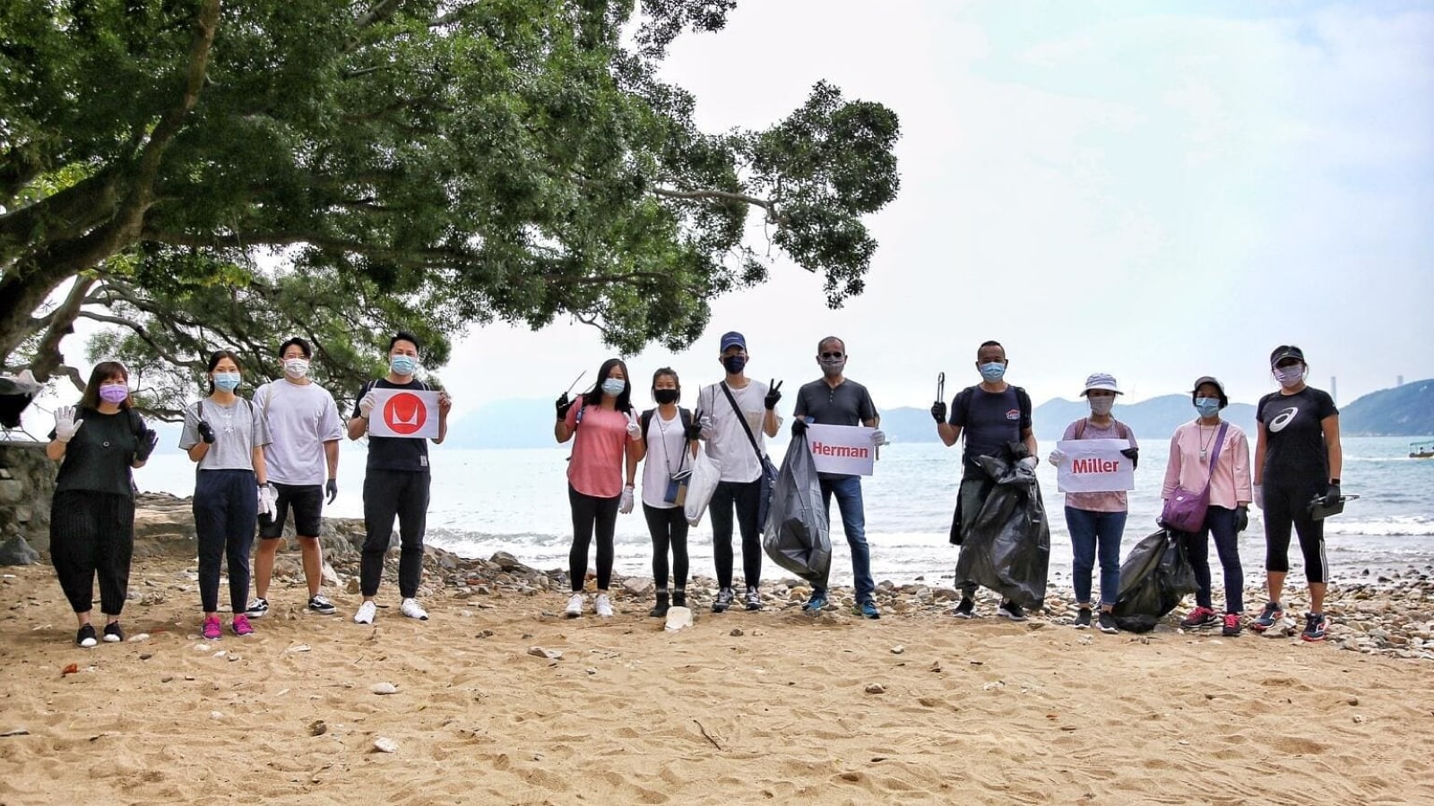 Twelve people are standing together on a beach holding rubbish bags that appear full with waste collected from the surrounding beach area.