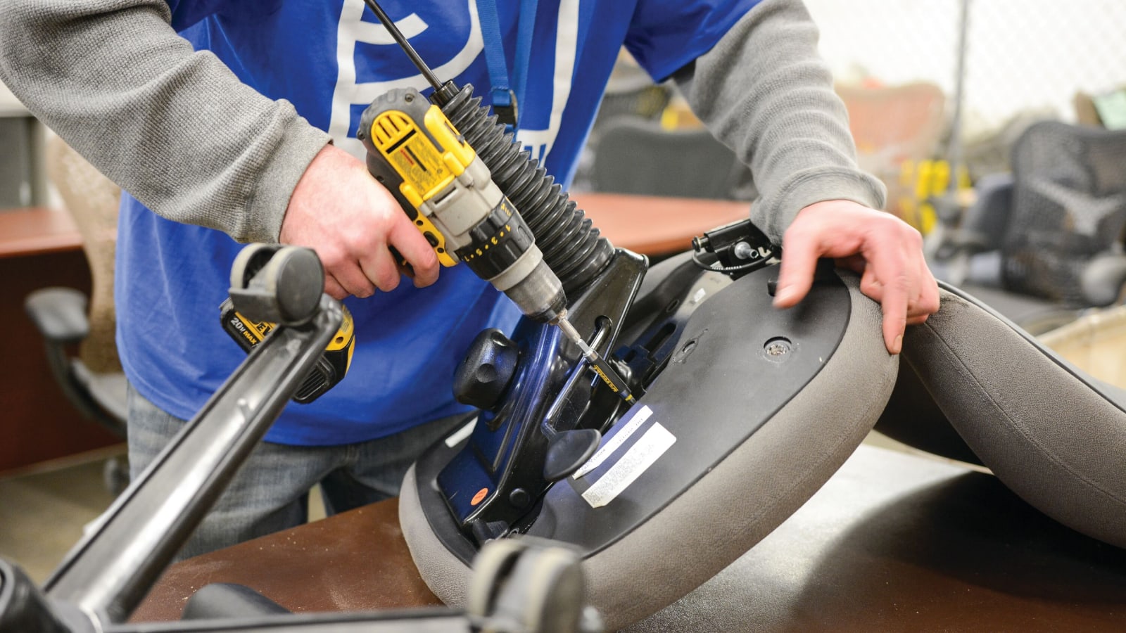 A close up view of a person holding the bottom, underside, section of an office chair and using a drill to secure parts during assembly. 