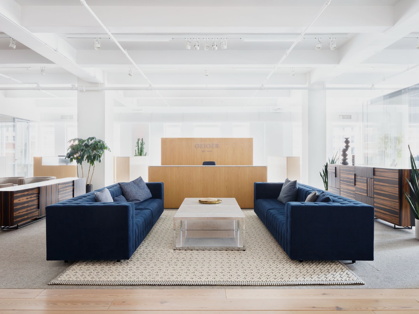 Eye-level view of Geiger reception lounge area with two Rapport Sofas in navy blue with a cube-shaped marble table with white marble surfaces and silver legs.