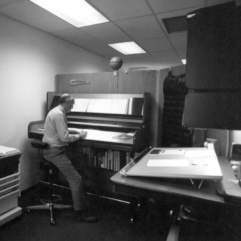 Robert Propst, l'inventeur du système Action Office, assis sur un siège haut devant un poste de travail debout.