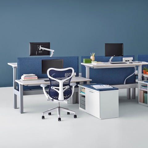 Adjacent workstations equipped with sit-to-stand surfaces, one positioned at seated height and one at standing height.