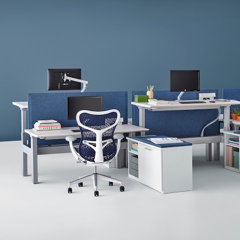 Adjacent workstations equipped with sit-to-stand surfaces, one positioned at seated height and one at standing height. Adjacent workstations equipped with sit-to-stand surfaces, one positioned at seated height and one at standing height.