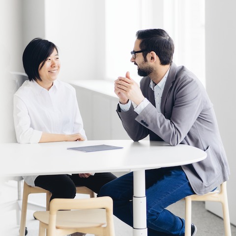 A woman and man share a laugh while seated at an oval table.