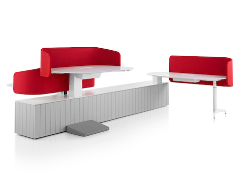 Una estación de trabajo Locale en gris con pantallas en género rojo y tres superficies de trabajo en escritorio elevado, uno a una altura para estar sentado y dos a una altura que permite trabajar de pie.