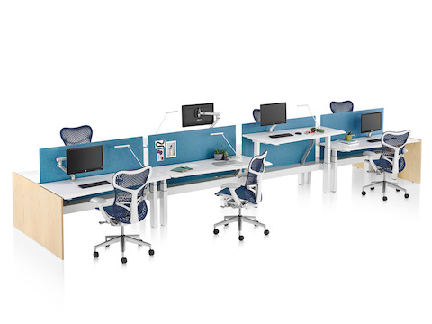 A Renew Link standing desk system with eight work surfaces, blue fabric screens, and blue and white Mirra 2 office chairs. Two of the work surfaces are raised to standing height.