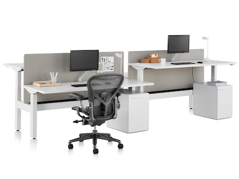 A Nevi Link standing desk system with four work surfaces, gray fabric screens, and a black Aeron office chair. One of the work surfaces is raised to standing height. 