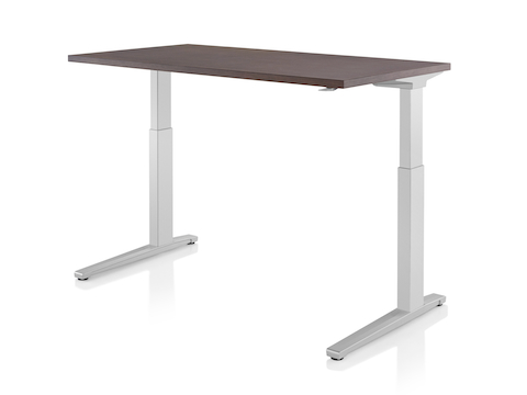 A Renew standing desk with light gray legs and dark wood work surface raised to standing height. A Renew standing desk with light gray legs and dark wood work surface raised to standing height.