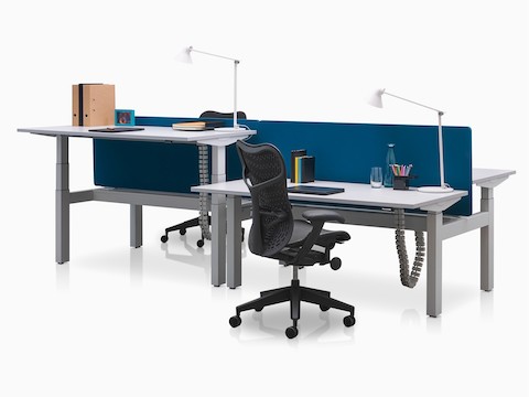 Mesas ajustáveis Ratio adjacentes, posicionadas nas alturas para trabalhar sentado e em pé com telas de privacidade azuis.