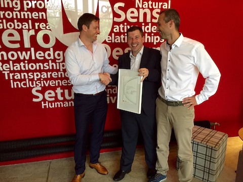 Two men congratulate a third, who holds a framed award.