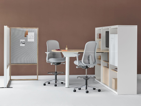 Parede de exibição do Grupo Canvas com banquetas Lino cinza e uma tela de limite cinza. Mesa de projetos Canvas Beam com cadeiras marrons.