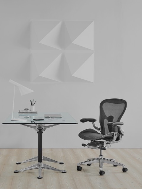 Uma mesa Burdick quadrada com tampo em vidro, usada como escrivaninha e complementada com uma cadeira de escritório Aeron preta.
