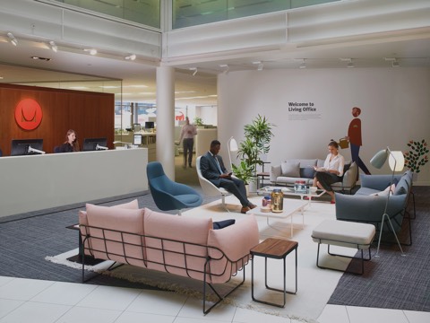 Duas pessoas aguardam em uma área de recepção da Herman Miller mobiliada com assentos para lounge em tons de azul, rosa e cinza.