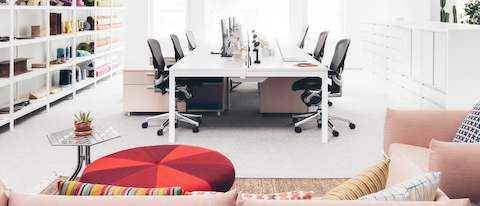 A view down the center of a bench workstation in an open office with black Aeron Chairs, shelving and storage units on either side.