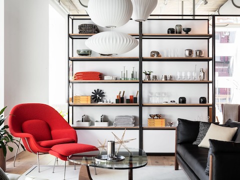 A lounge area with a red Womb Chair and Ottoman, a Noguchi Table, and a dark gray Emmy Sofa. 