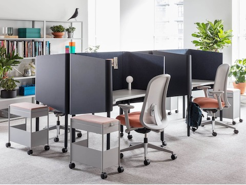 A bright workspace with four dark green OE1 Micro Pack desks, each with a red and gray Lino chair and gray OE1 Mobile Trolley. 