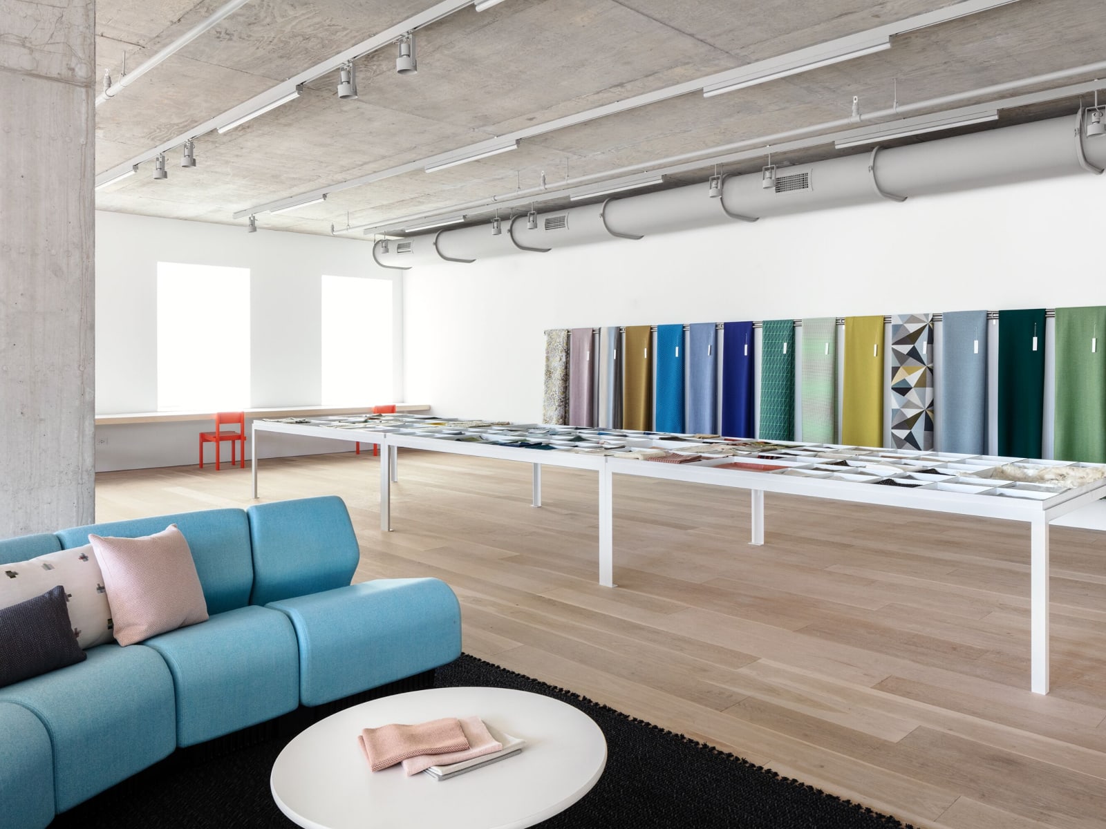 The Maharam Showroom at Fulton Market featuring a wall of colorful textiles, a white table covered with fabric swatches, and a blue Chadwick Sofa.
