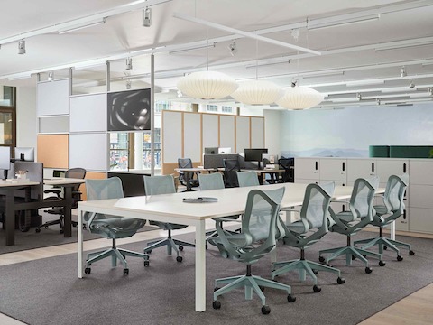 Grande table de travail accompagnée de sièges Cosm dans un environnement de bureau.