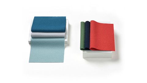 Two stacks of folded 100% recycled content fabric swatches in varying colors including neutrals, reds, greens, and blues.