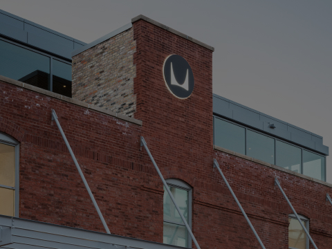 A view of the red brick exterior of the Fulton Market Showroom at dusk, with illuminated windows and a black Herman Miller sign.