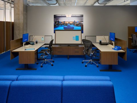 A large room with a blue sofa in foreground and two Canvas workstations and two Aeron office chairs.