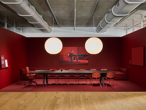 A large, rectangular Boa conference table lit with two hanging Nelson Bubble Lamps with red chairs in a red room.