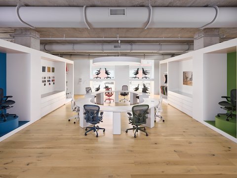 Eight ergonomic office chairs around a white, oval table in a large white room.