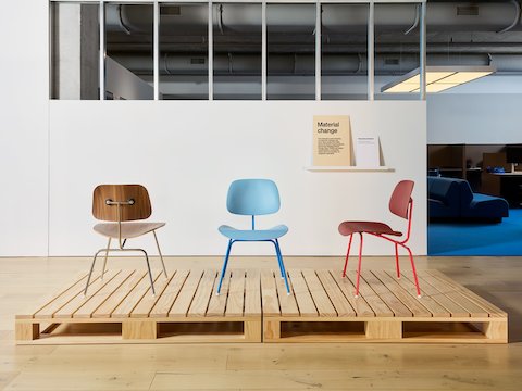 Two Eames Molded Plastic Dining chairs in blue and red and one Eames Molded Plywood Chair, all on a wood palette.